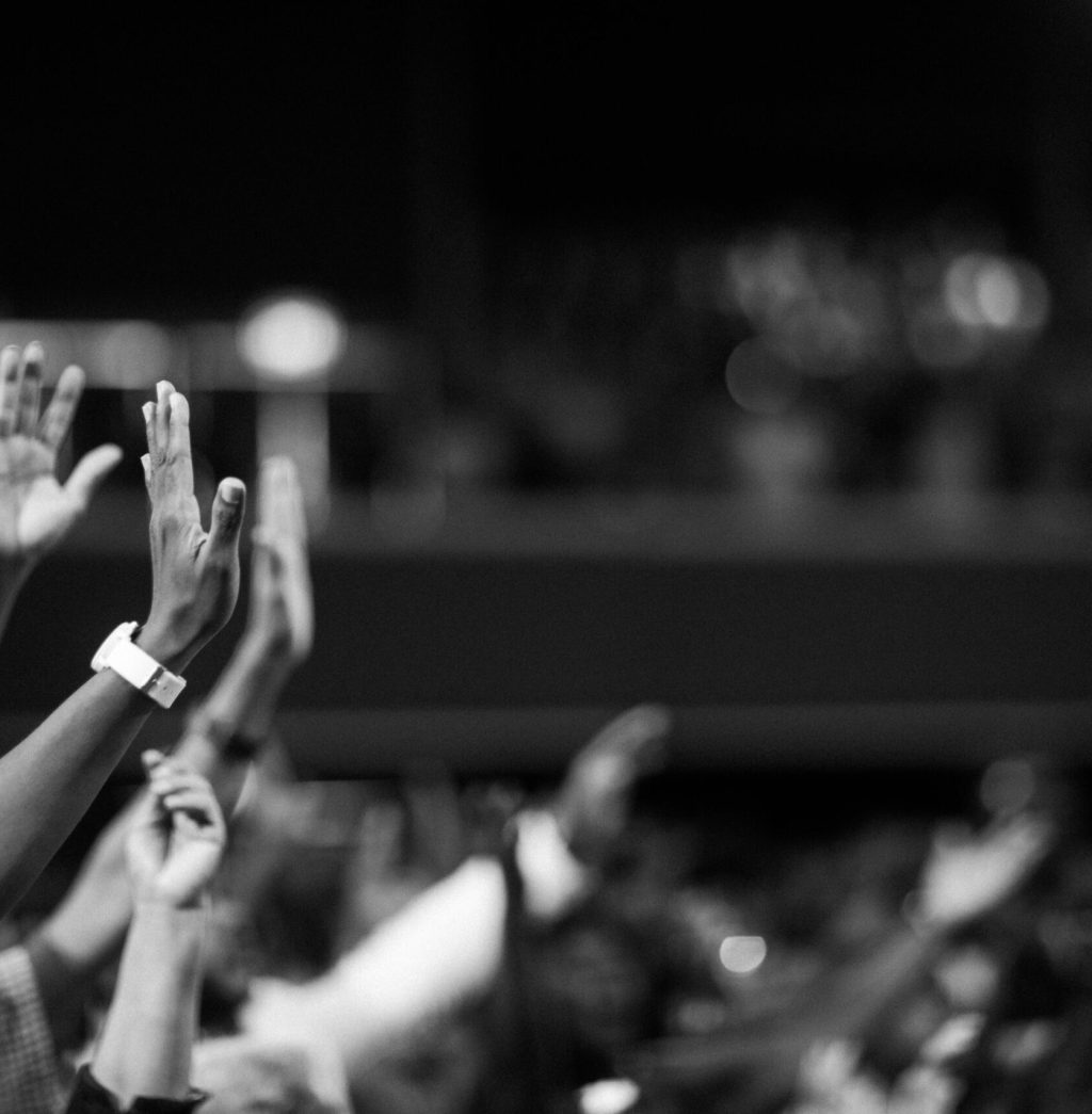 Black and white image of audience with hands raised, capturing concert energy.