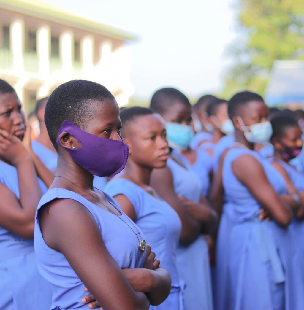 A group of students wearing blue uniforms and face masks gathered outdoors in Moyiri, Ghana.